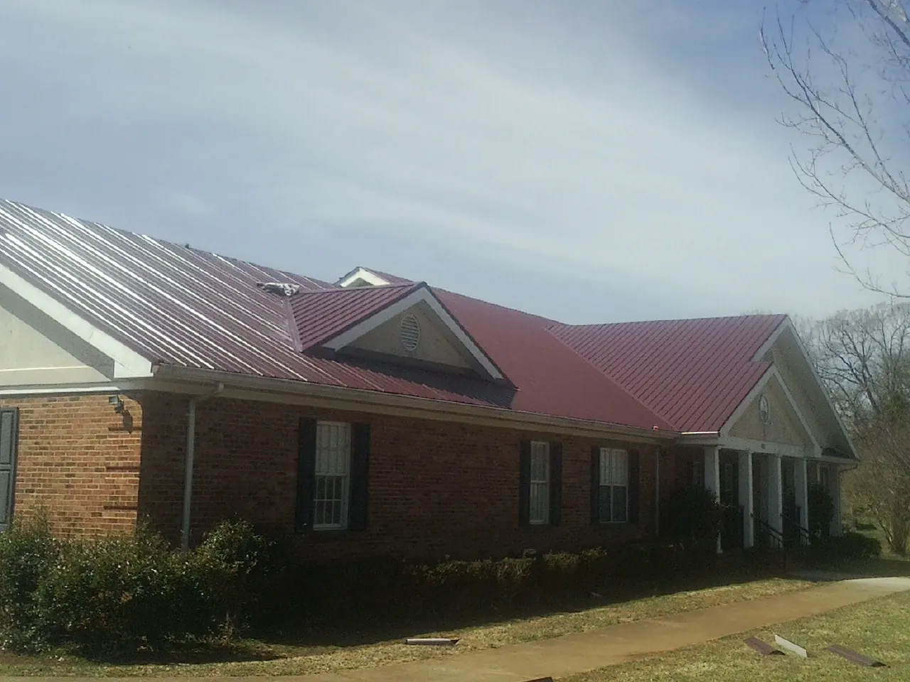 Red metal roof with gabled entries on a long brick building, from a Hail Damage Roof Repair job in Macks Inn