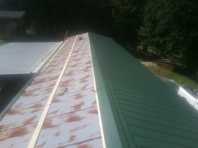 Old rusted panels beside newly installed green metal roofing — Wind Damage Roof Repair by Roofing Brothers in Macks Inn