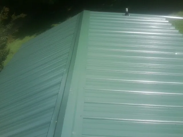 New green metal panels meeting at the ridge of a roof — Flat Roof Repair work by our crew in Macks Inn