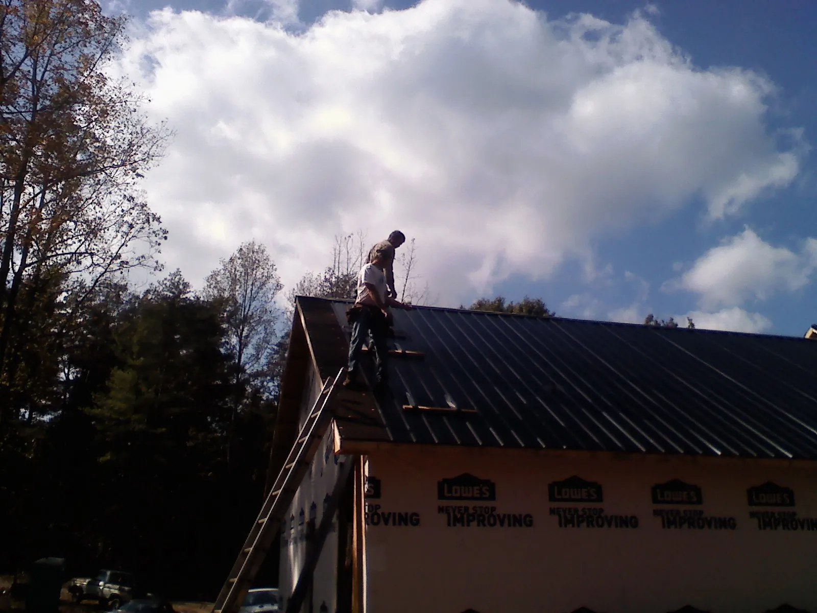 Roofer fastening dark metal panels high against a cloudy sky, from a Roof Inspection job in Macks Inn