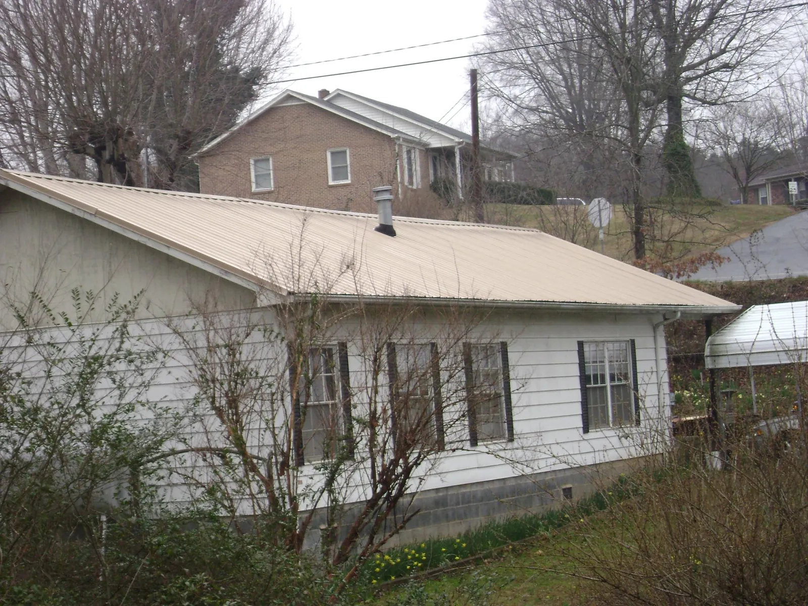 Tan metal roof on a white sided house set into a hillside — Commercial Roofing by Roofing Brothers in Macks Inn