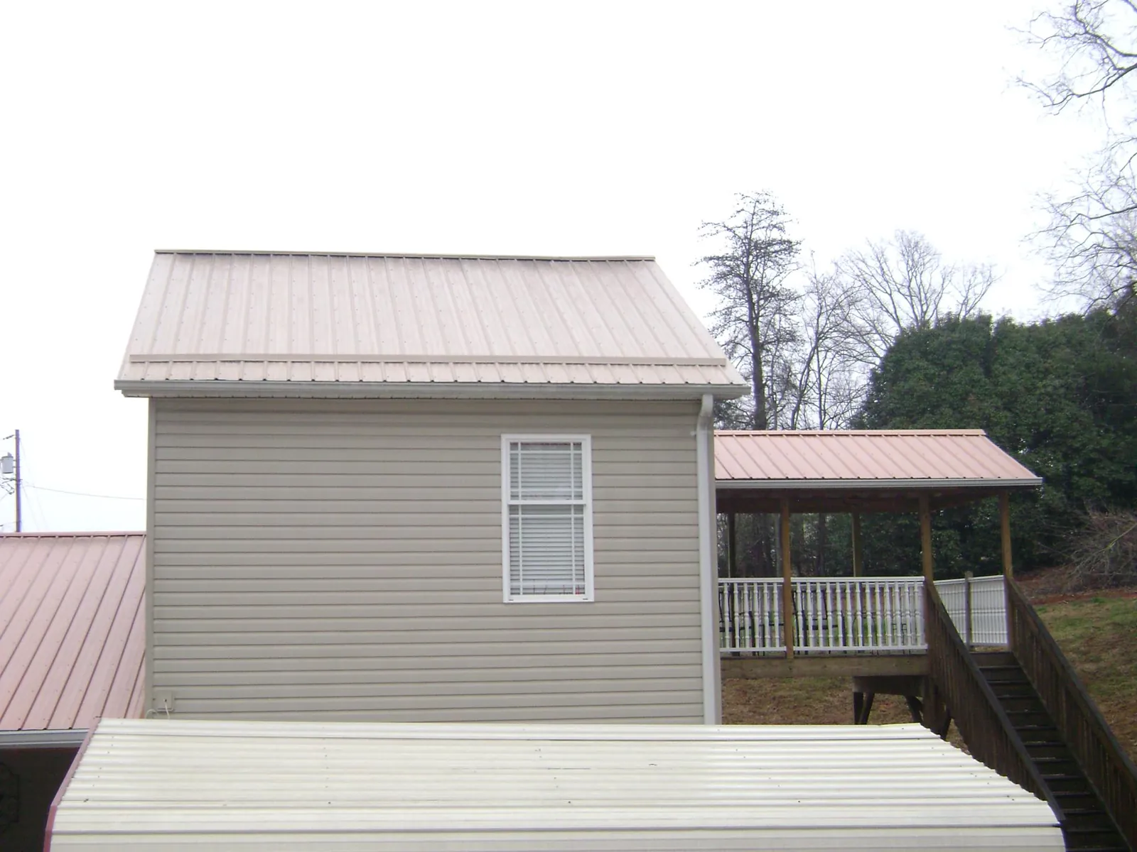 Tan metal roofs on a two story addition and attached porch, from a Roof Replacement job in Macks Inn